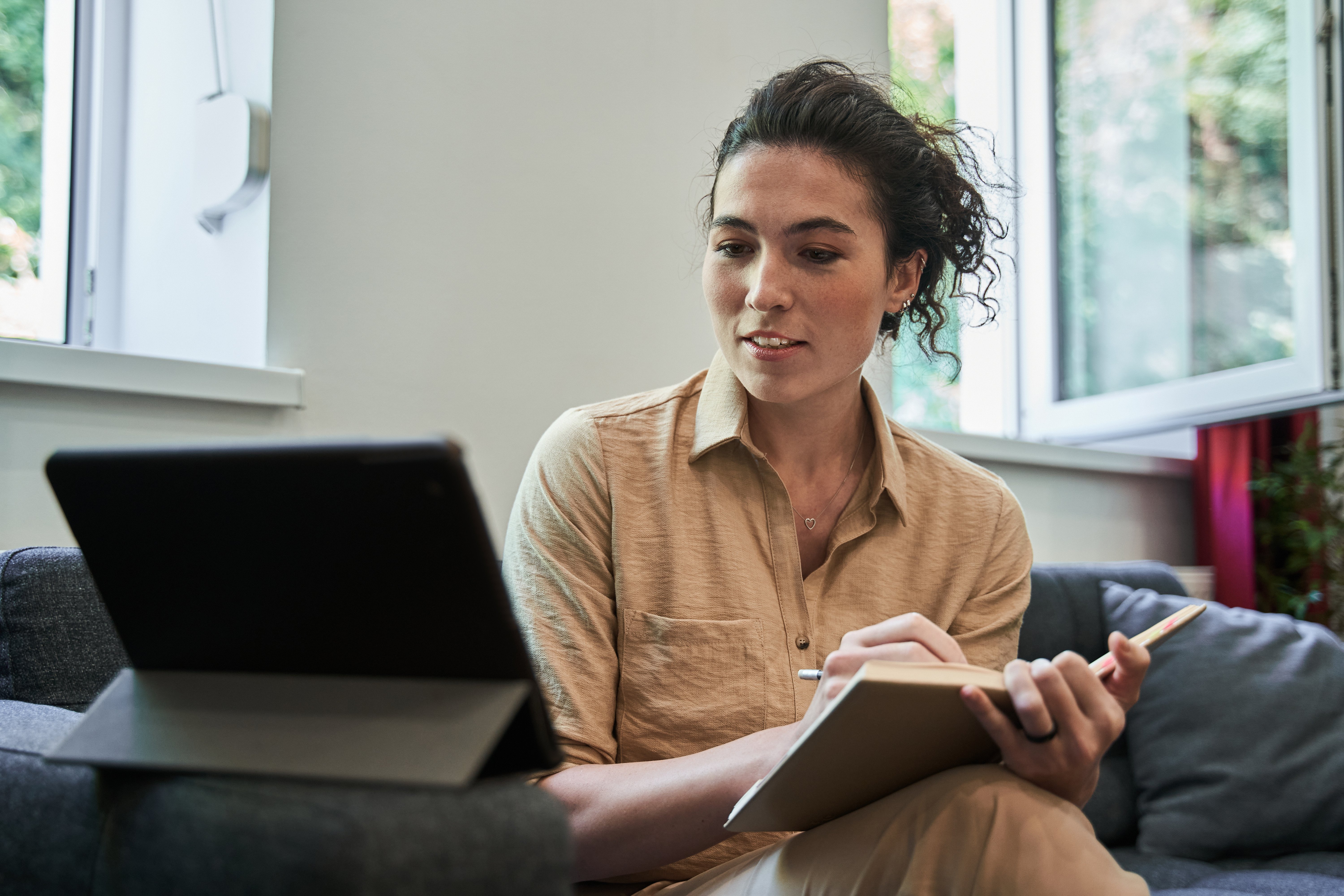 a lady sitting on the couch with pen and book in hand having a consultation on her iPad
