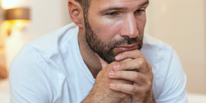 A young white man sitting with his hands on his chin thinking