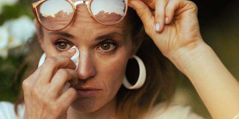 woman with glasses up her head cleaning her eyes with a wipe